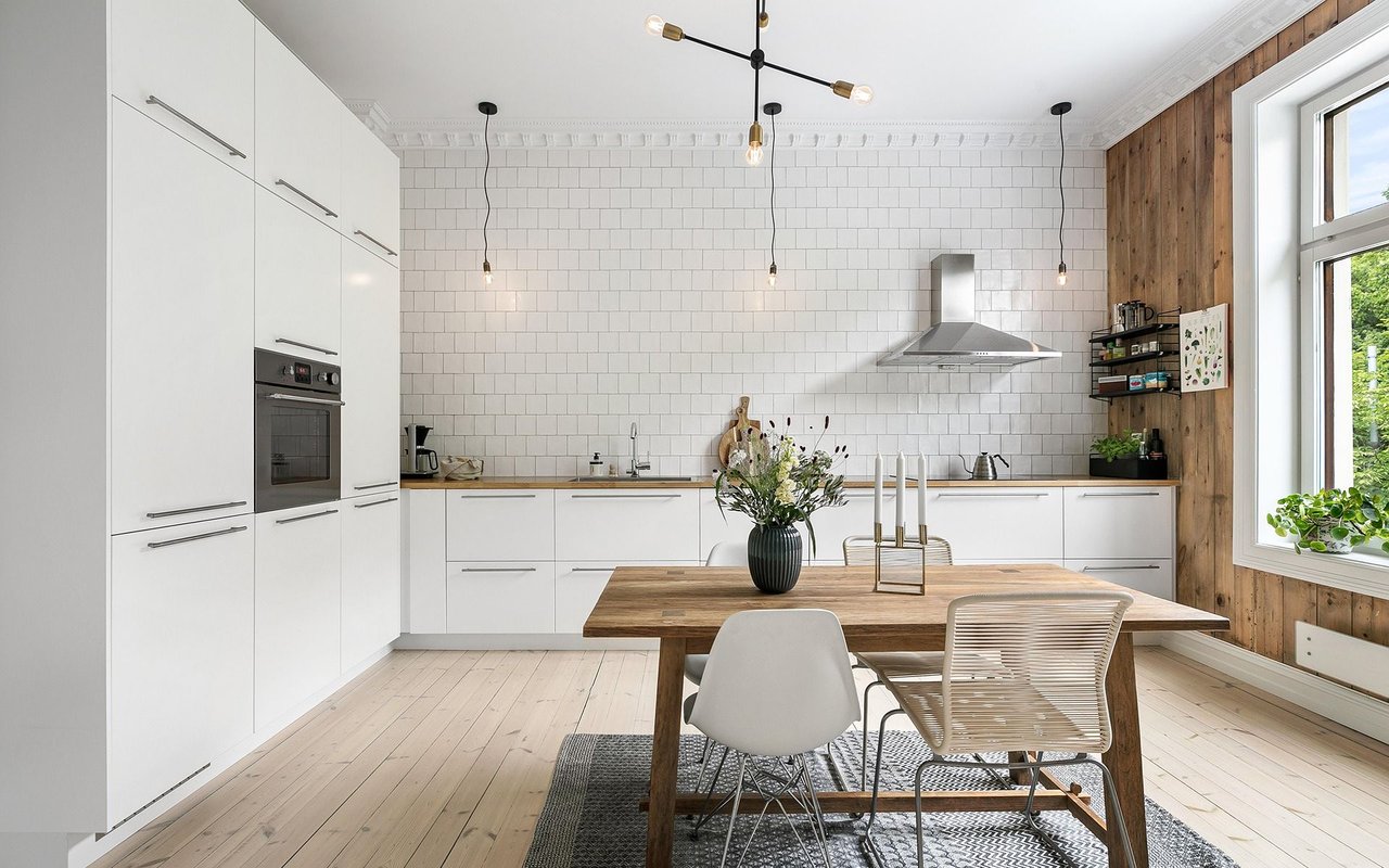 Modern white kitchen with subway tile, wood accents, and a dining table by large windows.