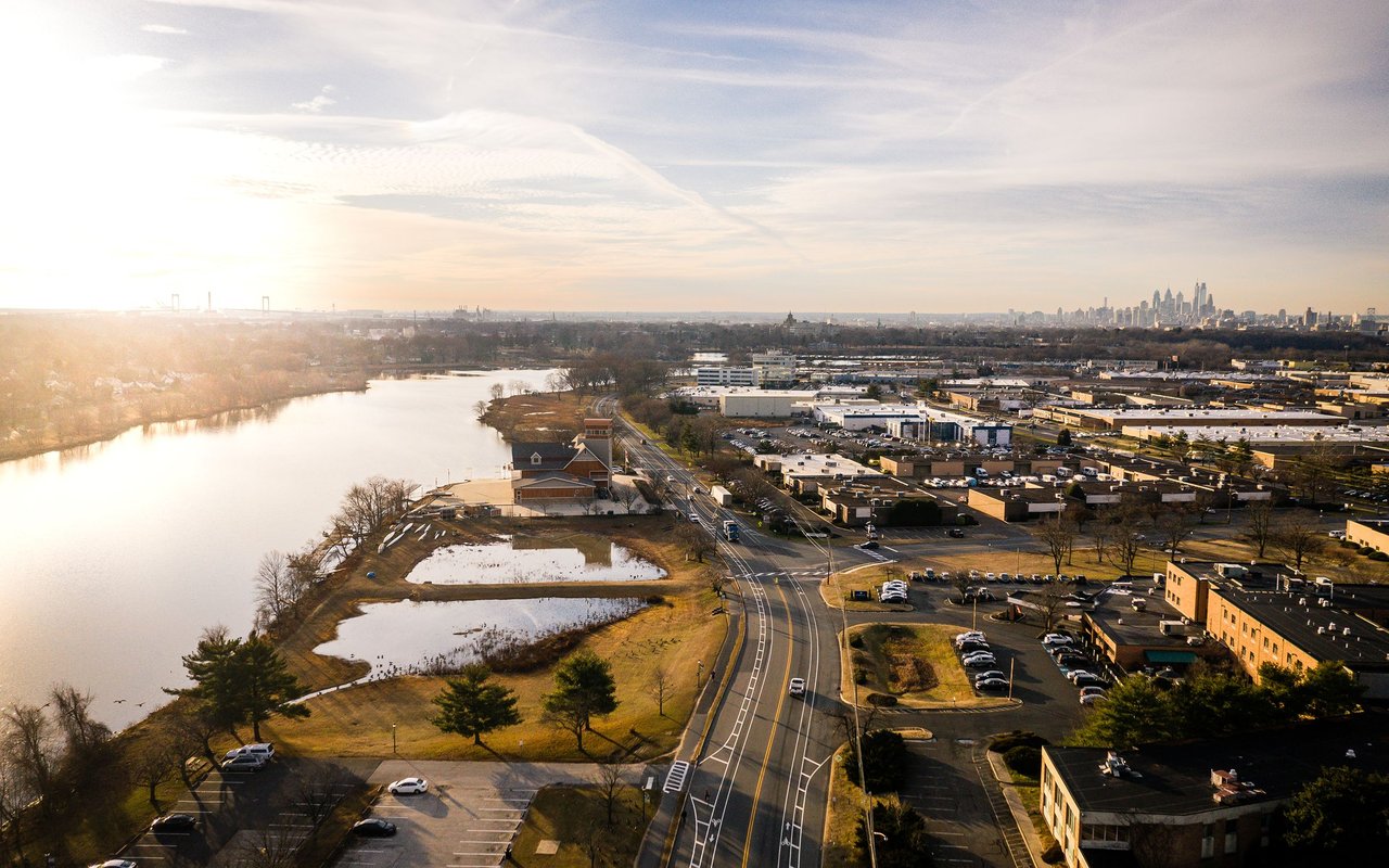 Aerial view of a river and commercial buildings with the Philadelphia skyline in the distance.