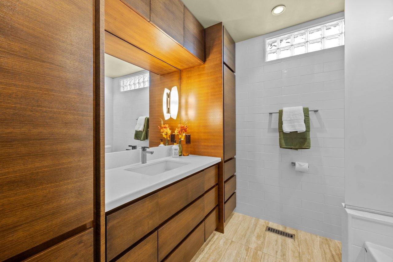 Bathroom with a long wood vanity, white tile walls, glass-block windows, and neatly hung towels.