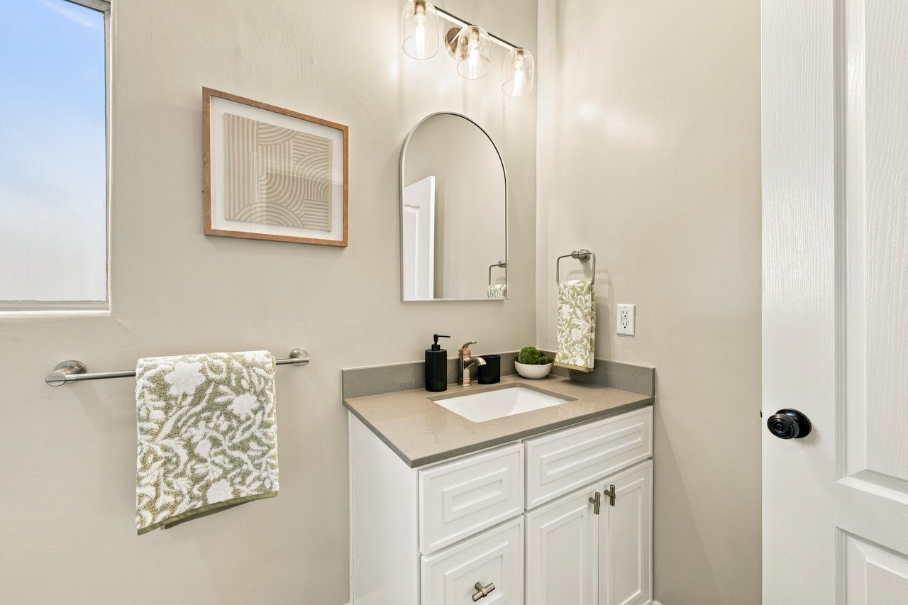Bathroom vanity with a gray countertop, arched mirror, and patterned towels.