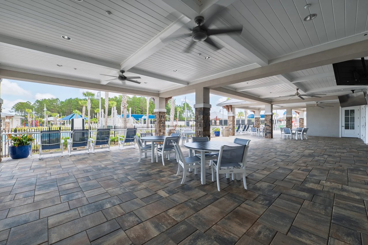 Covered community patio with ceiling fans, tiled flooring, and seating beside a playground.