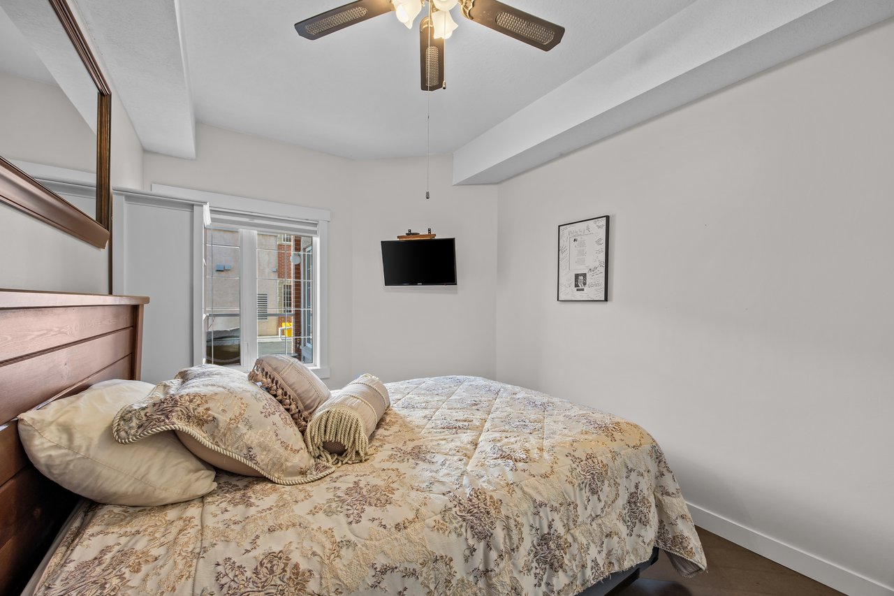 Furnished bedroom with a floral-quilted bed, mirrored closet door, and wall-mounted television.