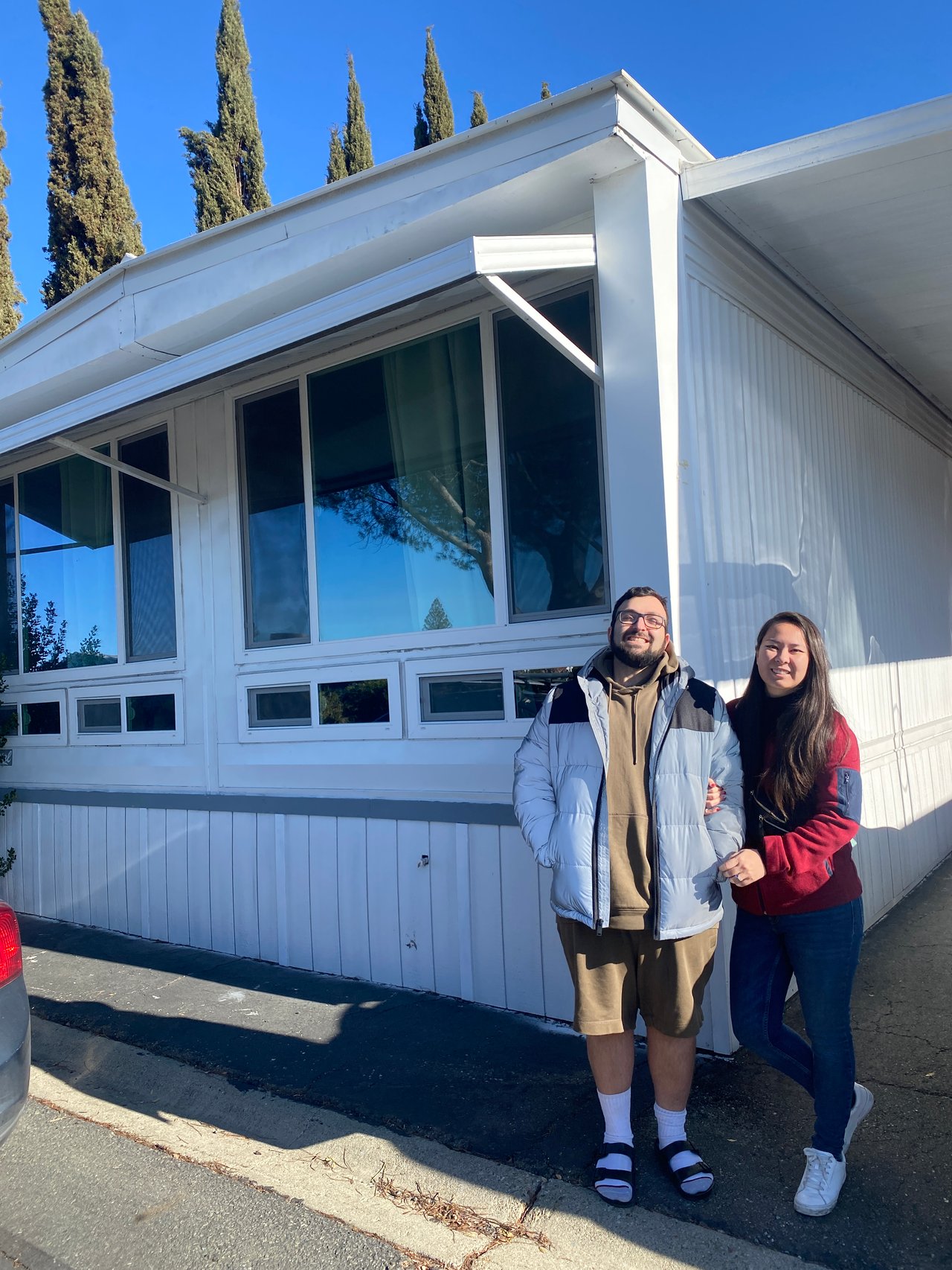 Two clients stand together outside a white home with a sharply angled roof.