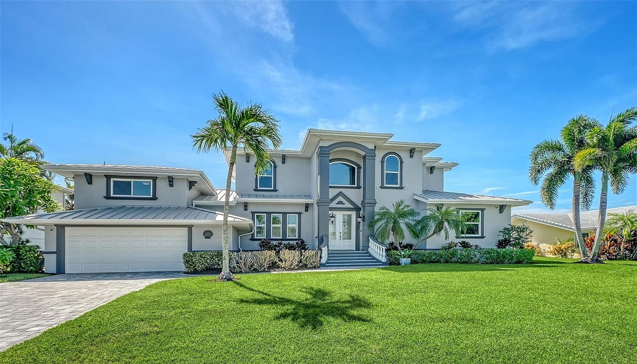 Two-story gray home with a metal roof, attached garage, palm trees, and broad green lawn.