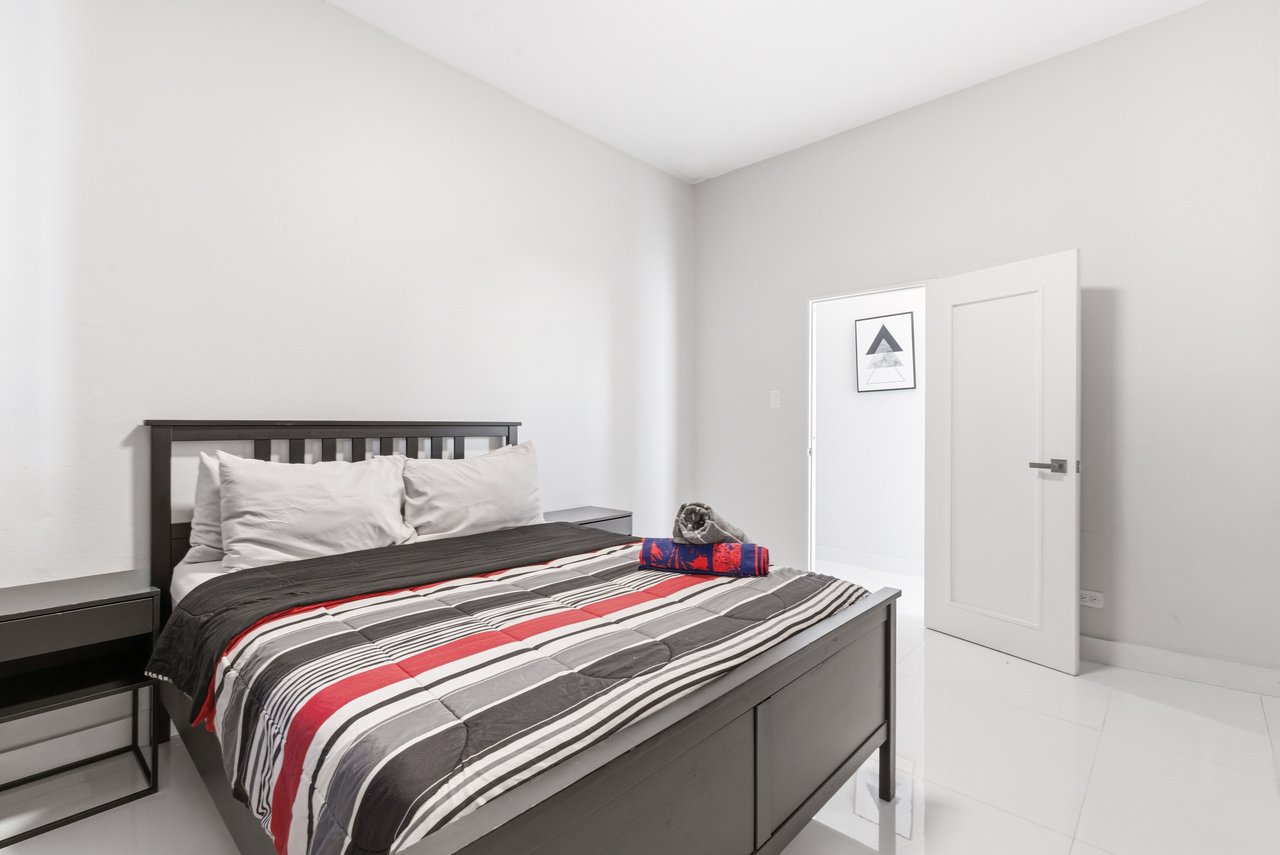 Furnished bedroom with a dark wood bed, red-and-gray striped bedding, and an open white door.