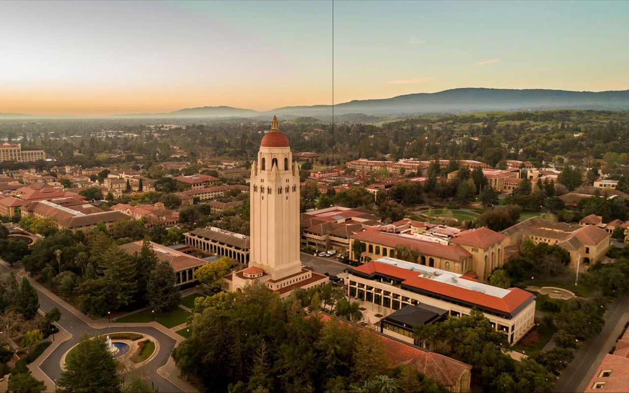 Aerial view of Stanford campus with Hoover Tower and wooded hills at golden hour.