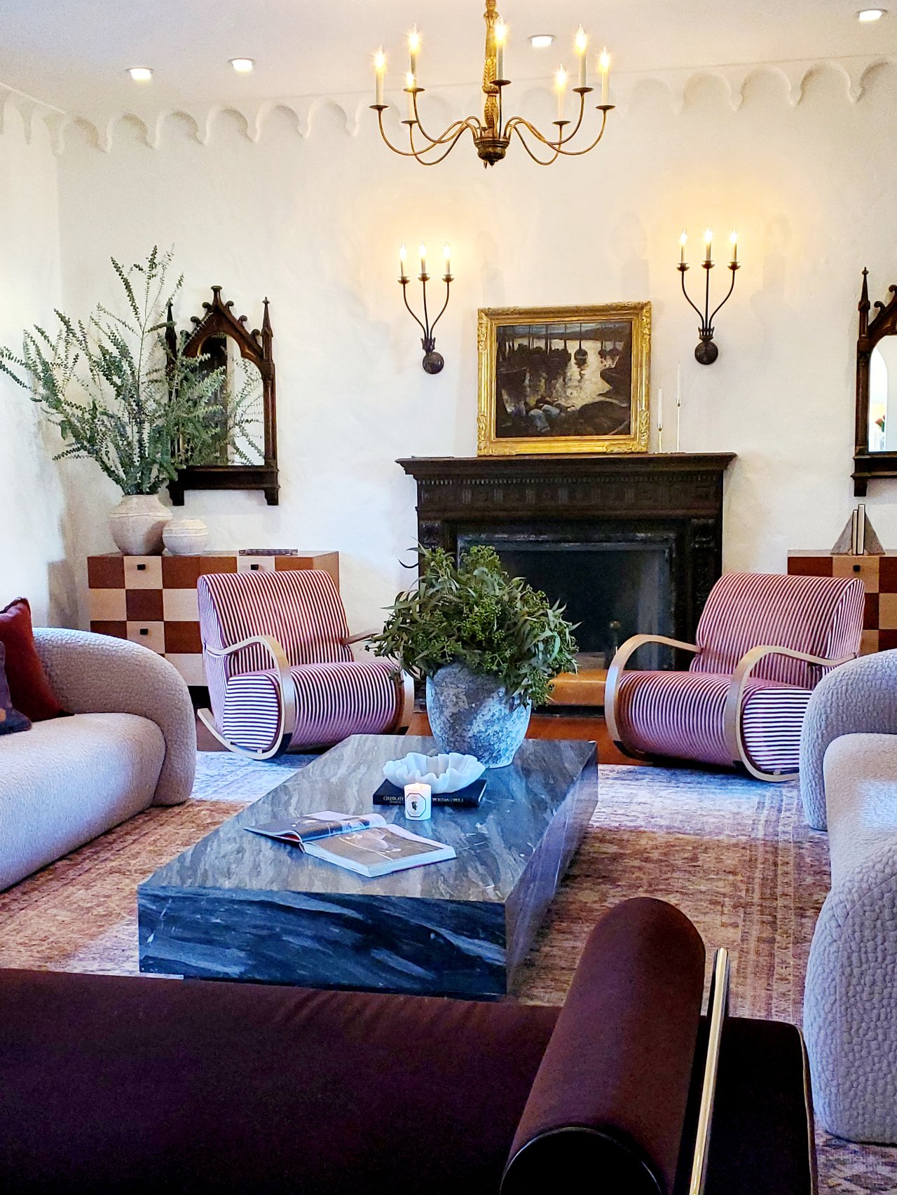 Elegant living room with chandelier, black fireplace, striped chairs, and large marble coffee table.