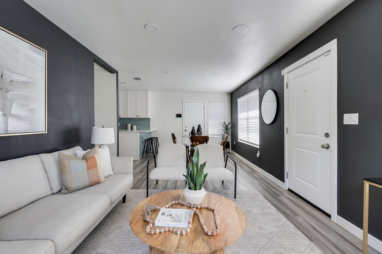 Staged living room with a light sectional, round wood coffee table, charcoal walls, and an open kitchen.