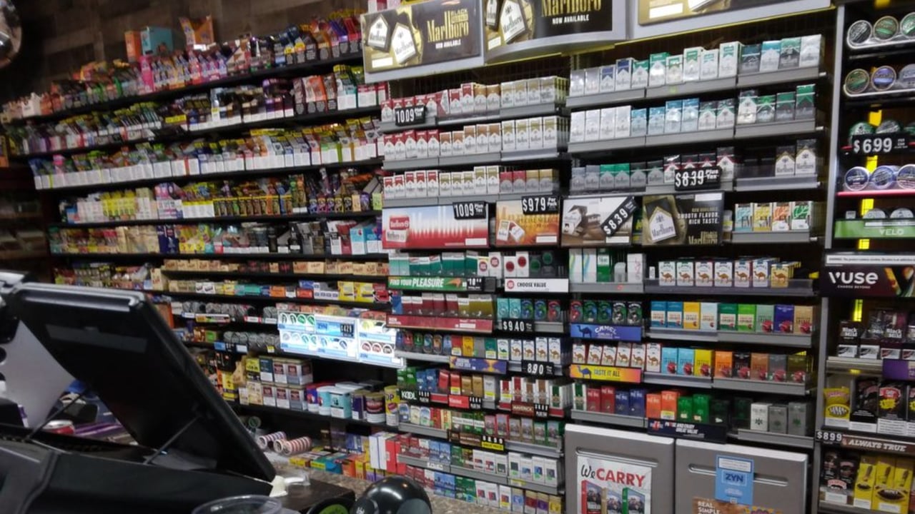 Convenience store tobacco counter stocked with cigarette packs and vaping products, with prices displayed on the shelves.