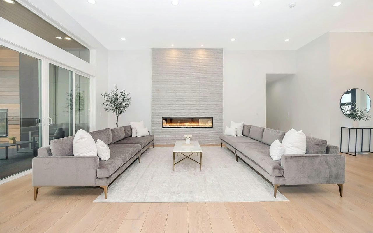 Bright minimalist living room with two matching grey sofas, a marble coffee table, an area rug, light wood floors, and a sleek linear gas fireplace.