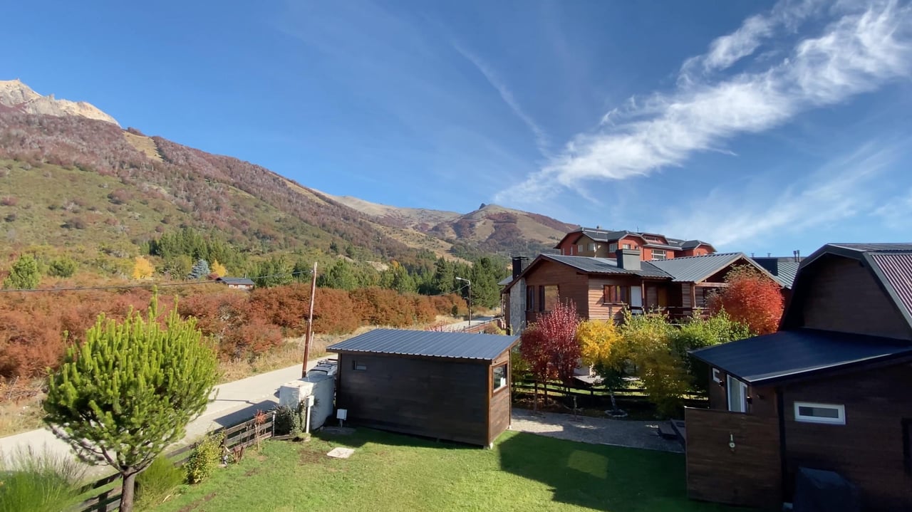 Timber cabins on a grassy property below an autumn-colored mountain slope.
