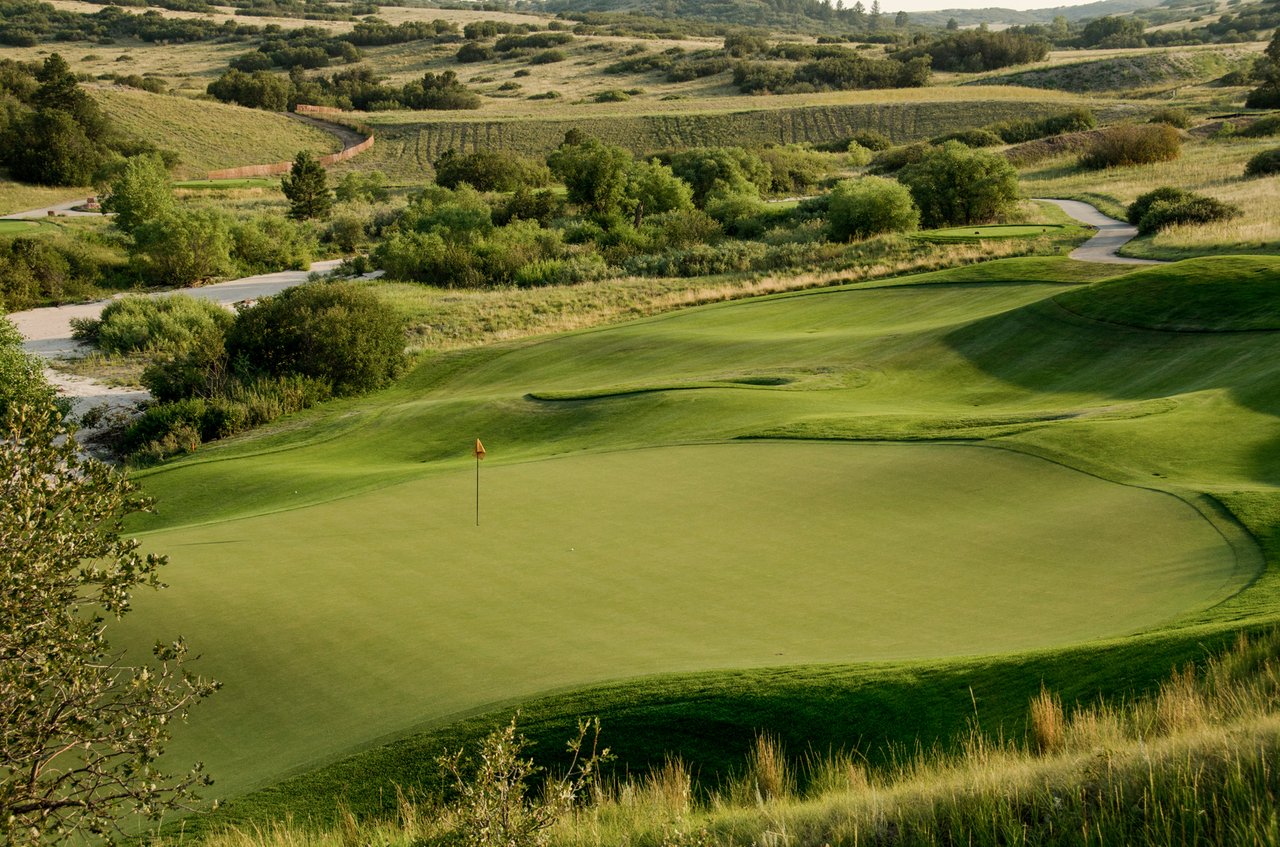 The Club at Pradera golf green and flagstick amid rolling hills and native grasses.