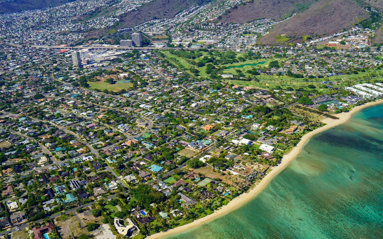 Aerial view of coastal homes, a golf course, and ridges beside turquoise water.