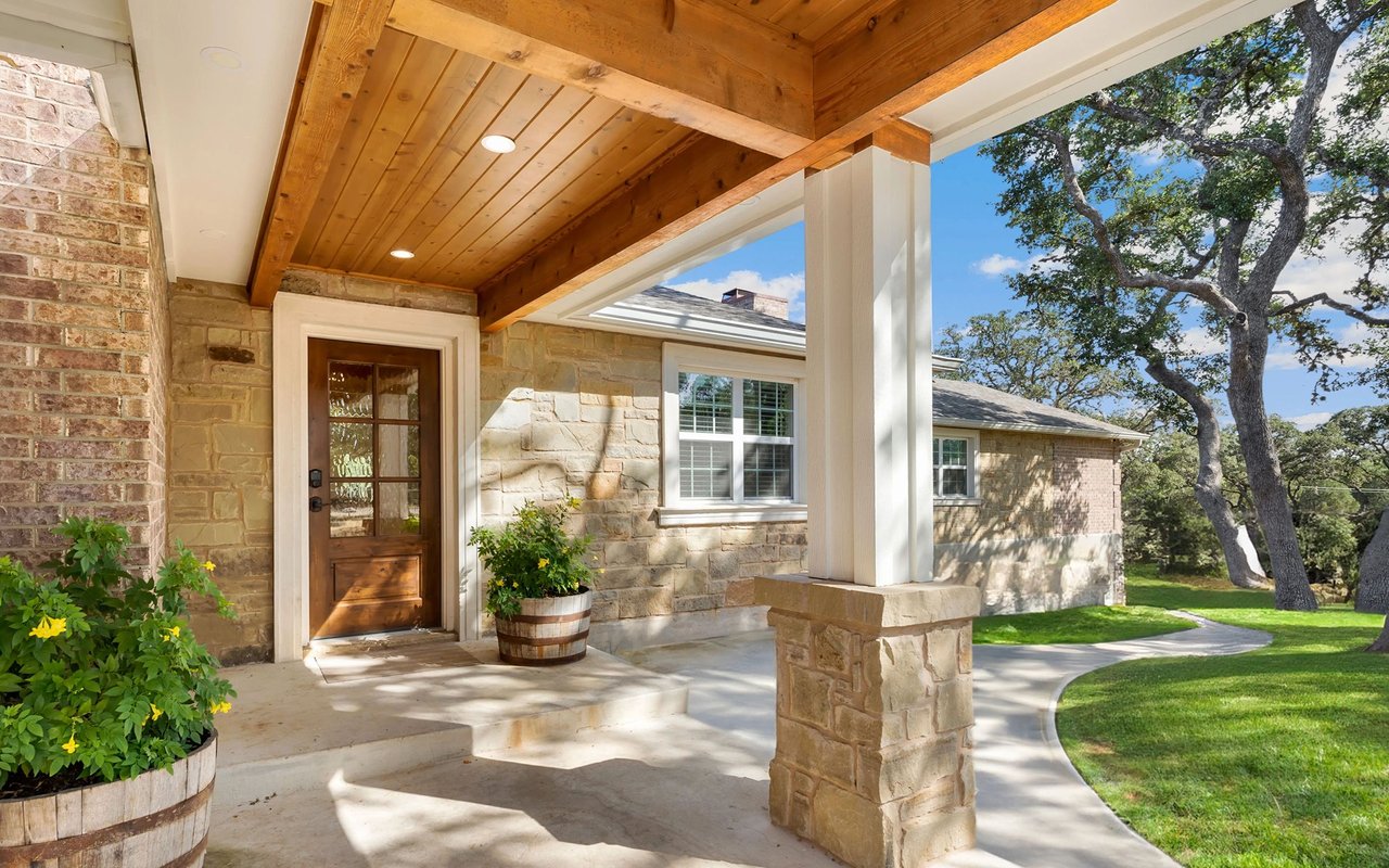 Stone home entrance with a timber-ceiling porch, wooden door, and curved walkway through the lawn.
