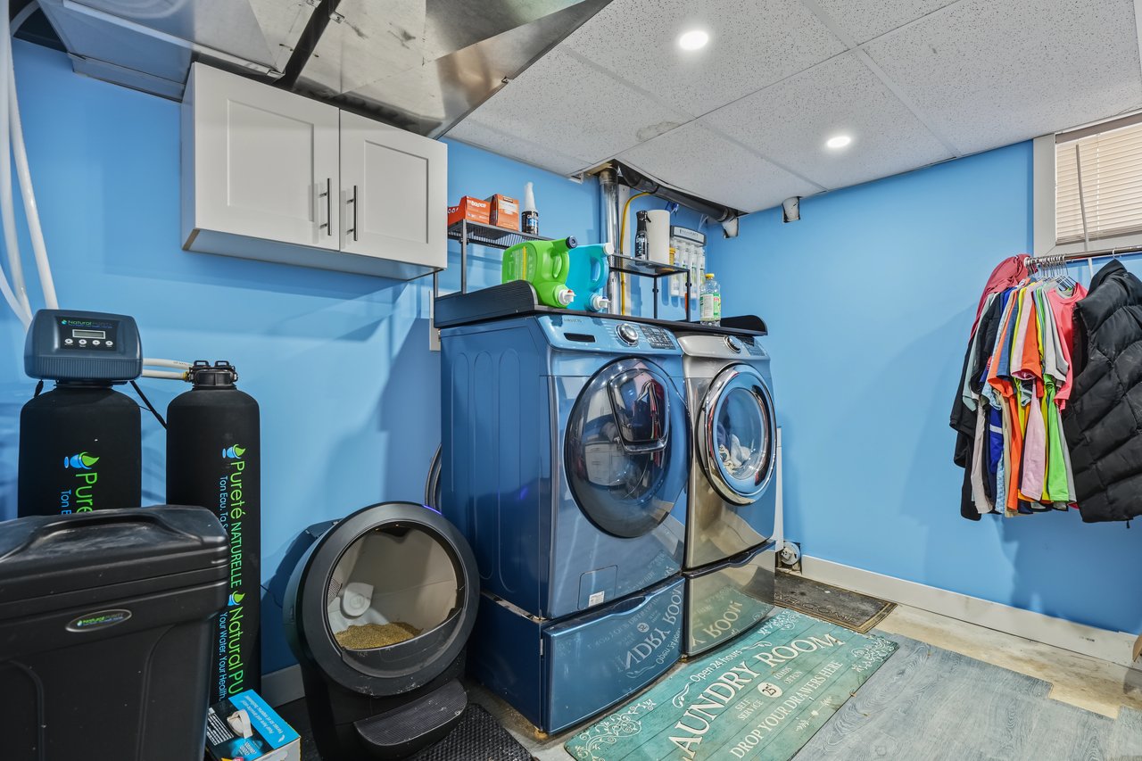 Laundry room with blue walls, front-loading washer and dryer, and water treatment tanks.