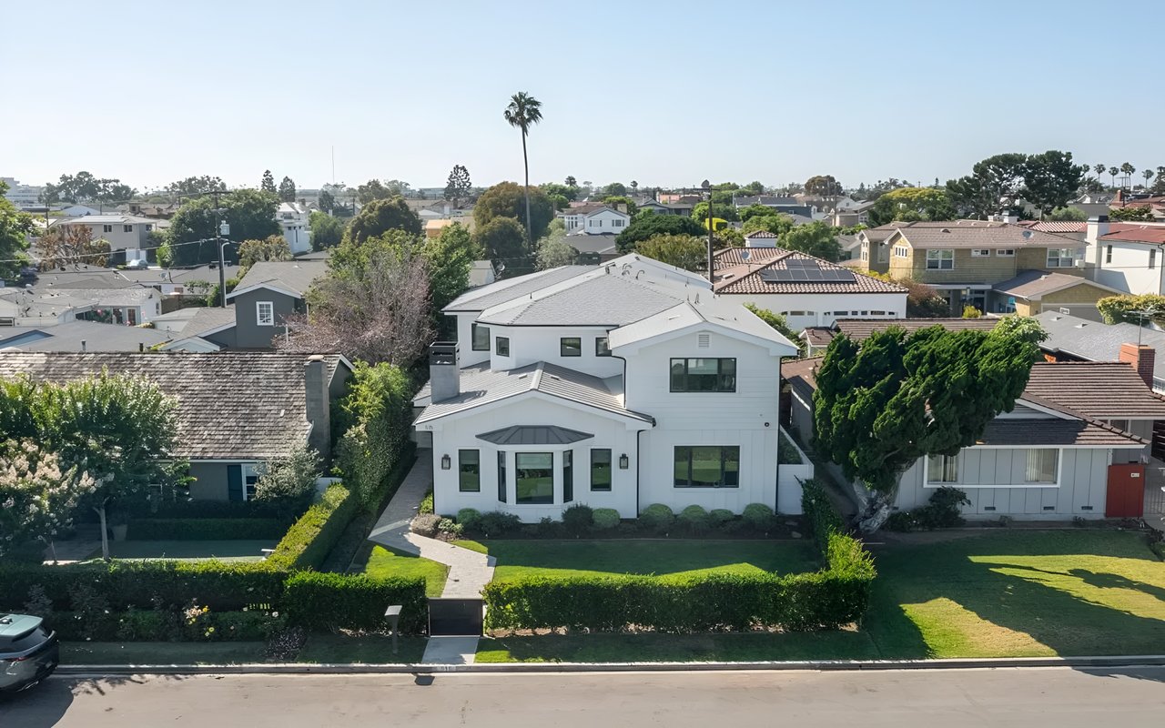 An aerial view of a white, modern two-story home with a manicured front lawn in a residential neighborhood in Newport Beach.
