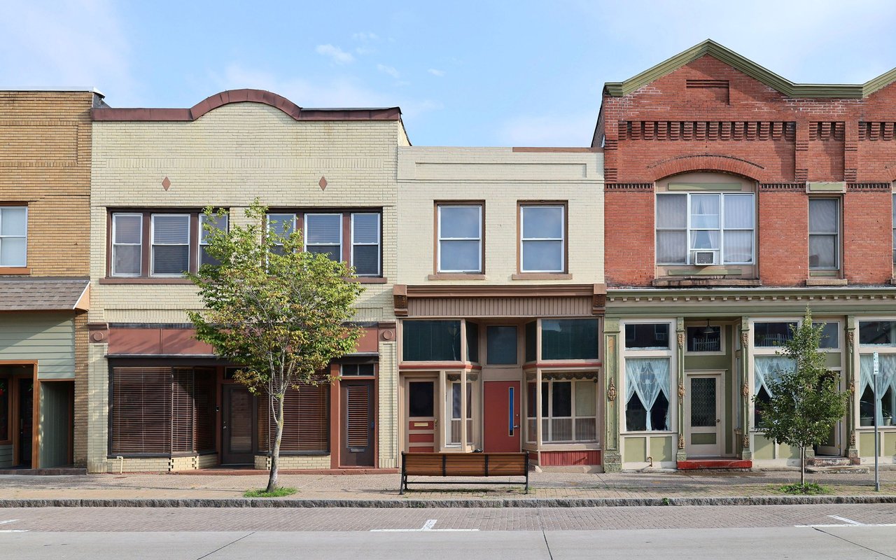 Historic brick storefronts line a Deep Deuce street beside a sidewalk bench and trees.