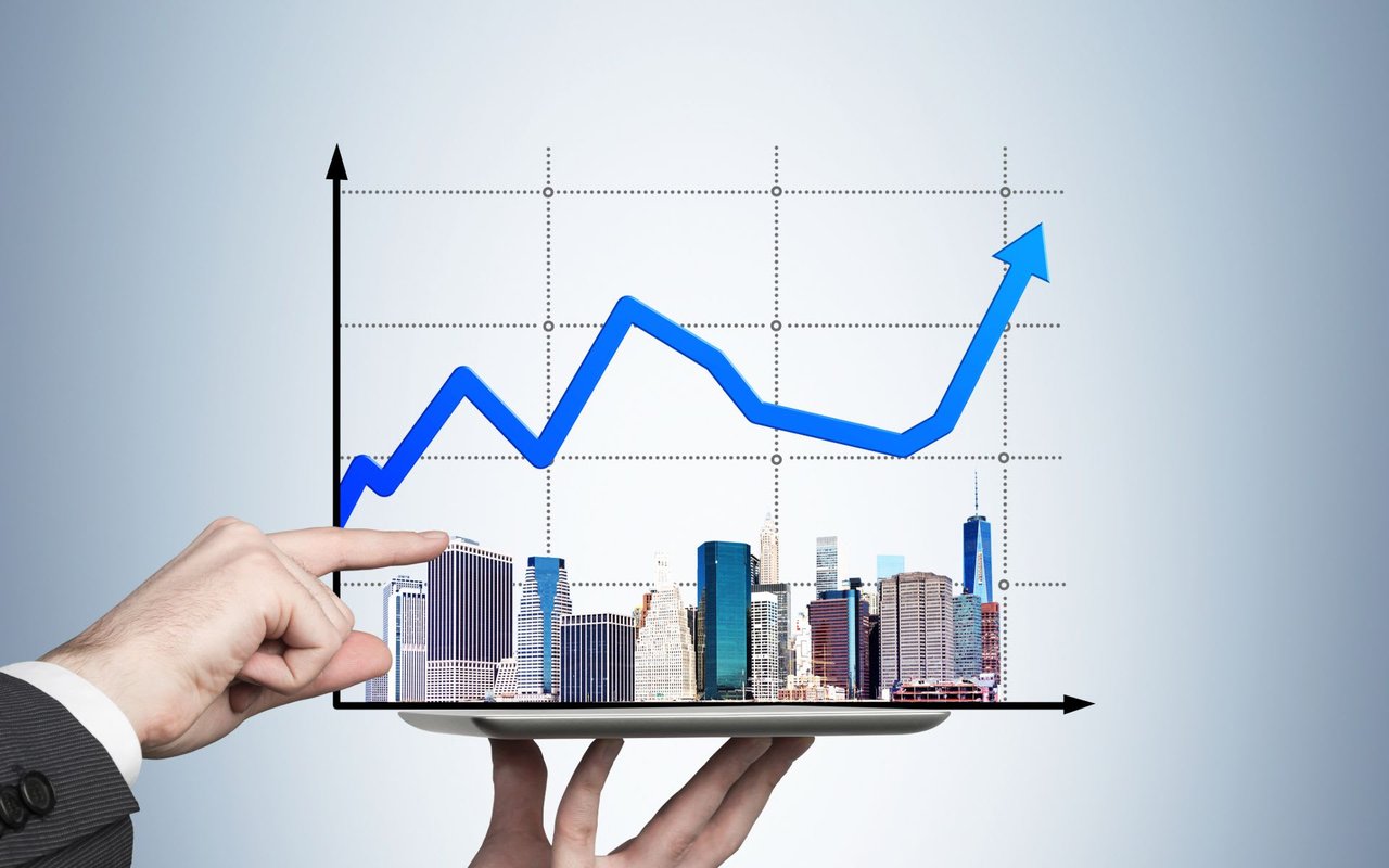 A hand holds a tablet displaying a city skyline beneath a rising blue chart.