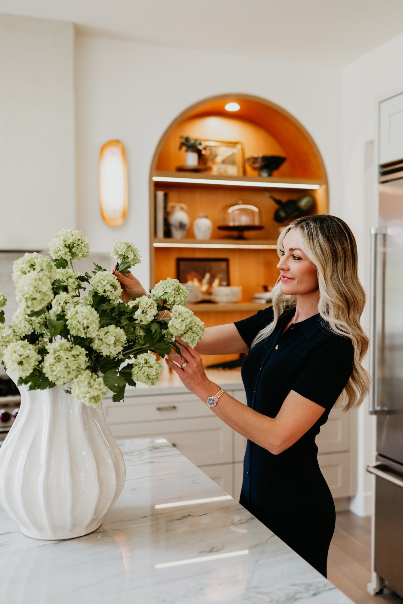 Kaylee Gallagher arranging white flowers in a vase in a bright kitchen.