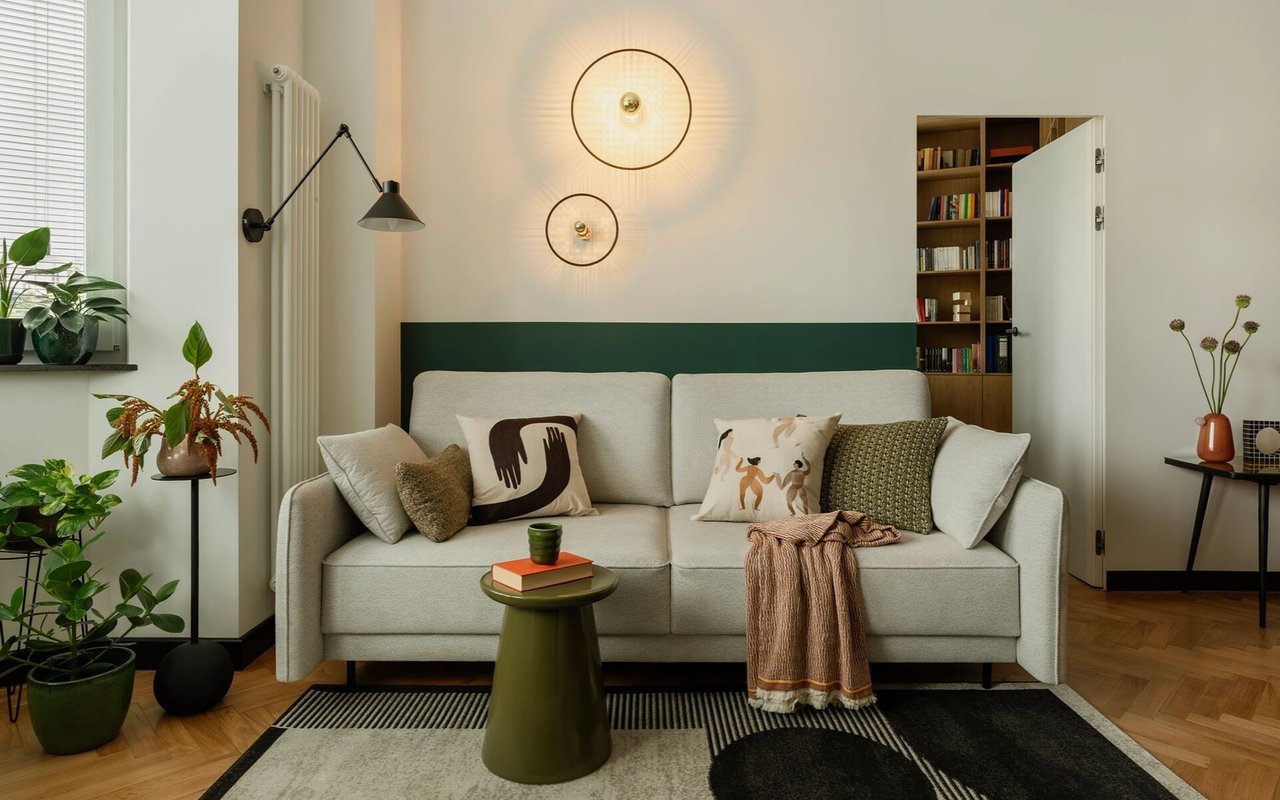 Staged living room with a light gray sofa, green accent wall, circular sconces, built-in bookshelves, and leafy plants.