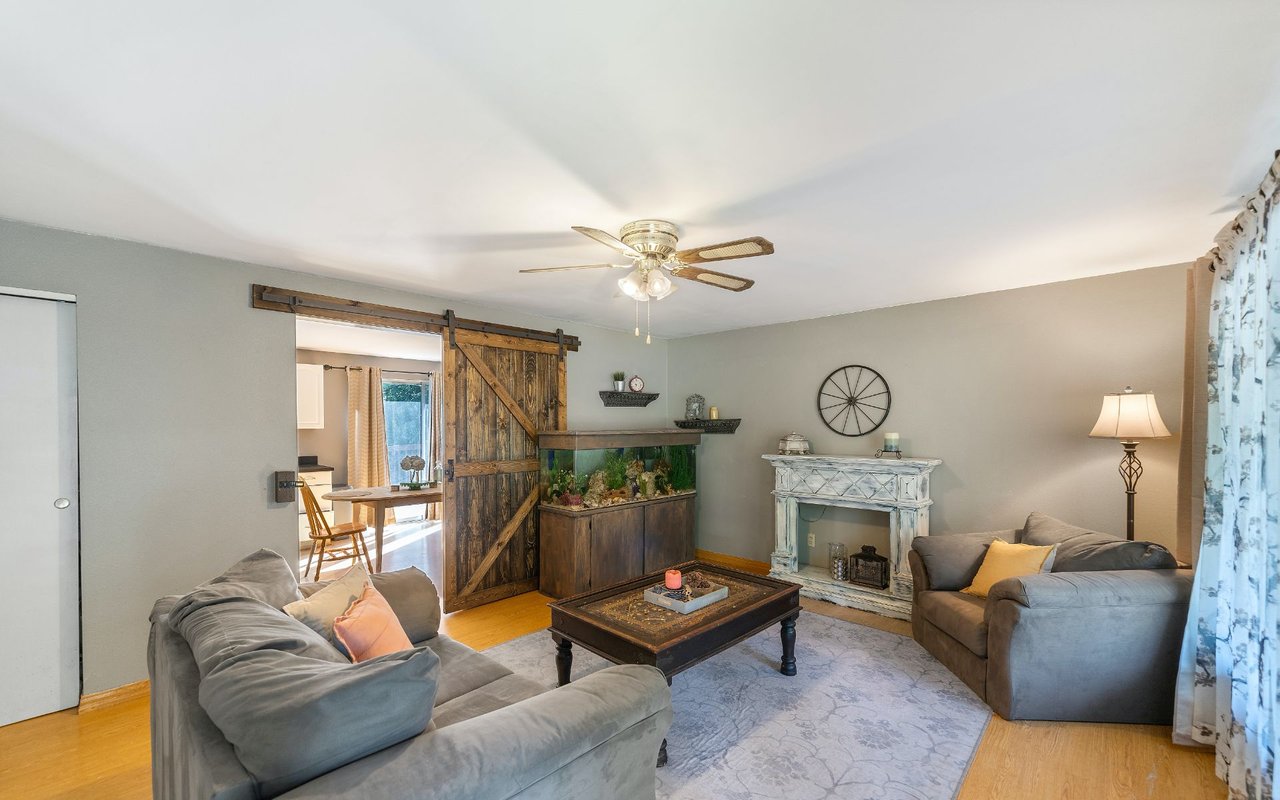 Living room with gray sofas, a rustic sliding barn door, a large aquarium, and a decorative fireplace mantel.
