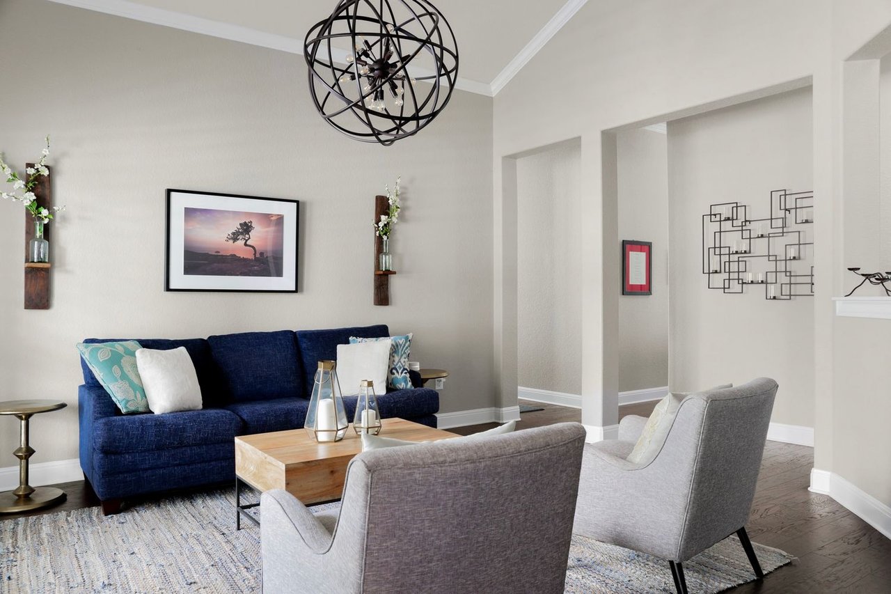 Staged living room with a navy sofa, gray armchairs, and black globe chandelier.
