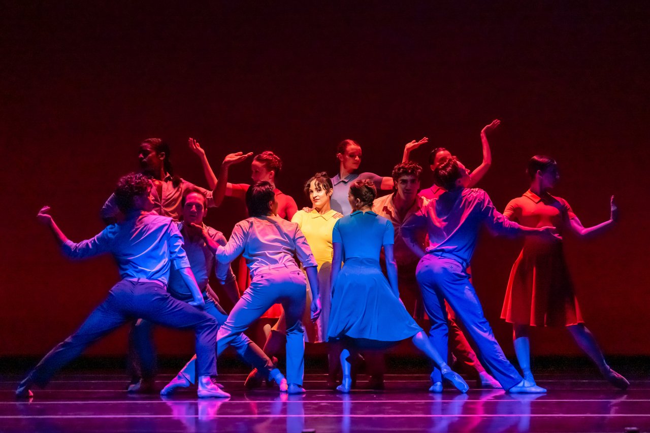 Ballet dancers performing on stage under red and blue lights.