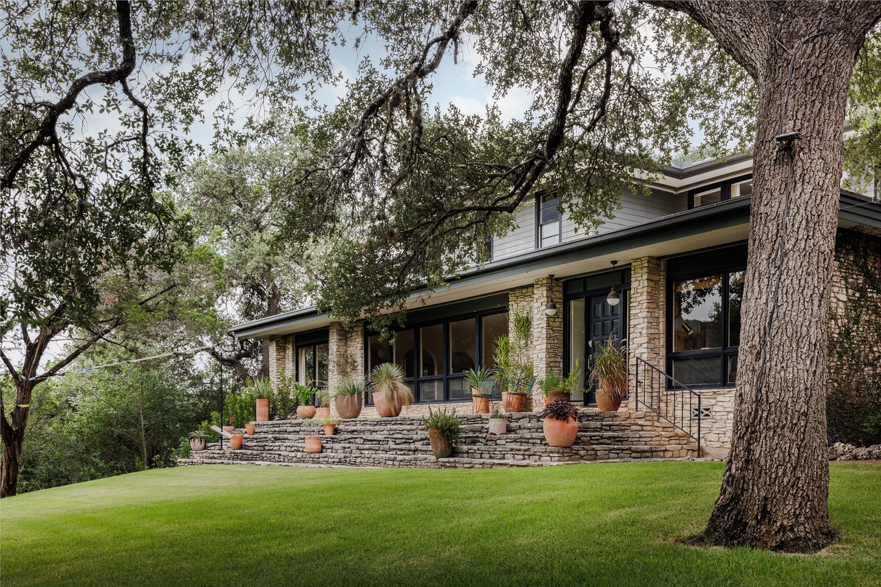 Two-story stone-fronted home with plant-lined steps beneath mature trees.