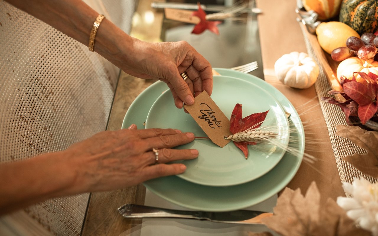 Hands arrange a Thanksgiving place setting with mint-green plates and a “Thankful” card.