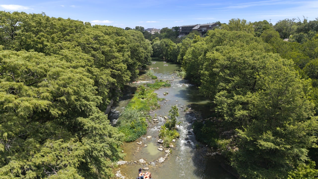 Aerial view of the Guadalupe River in New Braunfels, TX, with cypress trees along both banks.