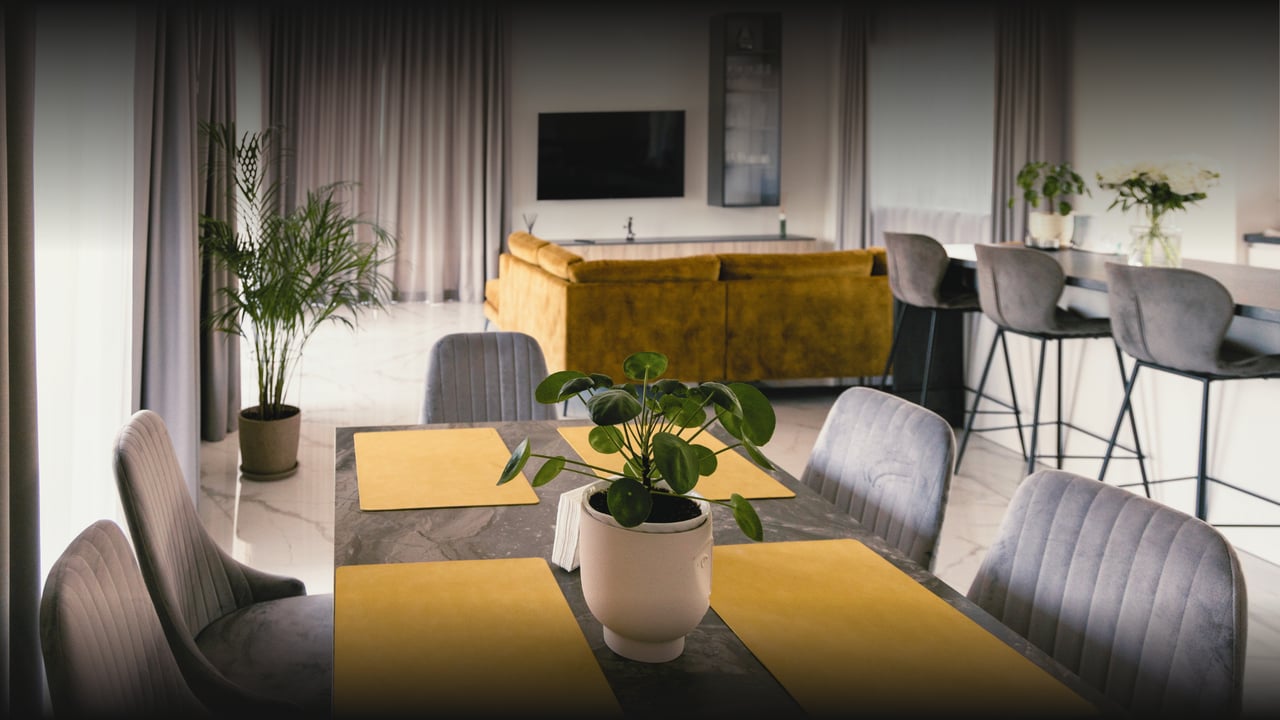Open-plan dining and living room with a marble table, gray chairs, and mustard-colored sofa.