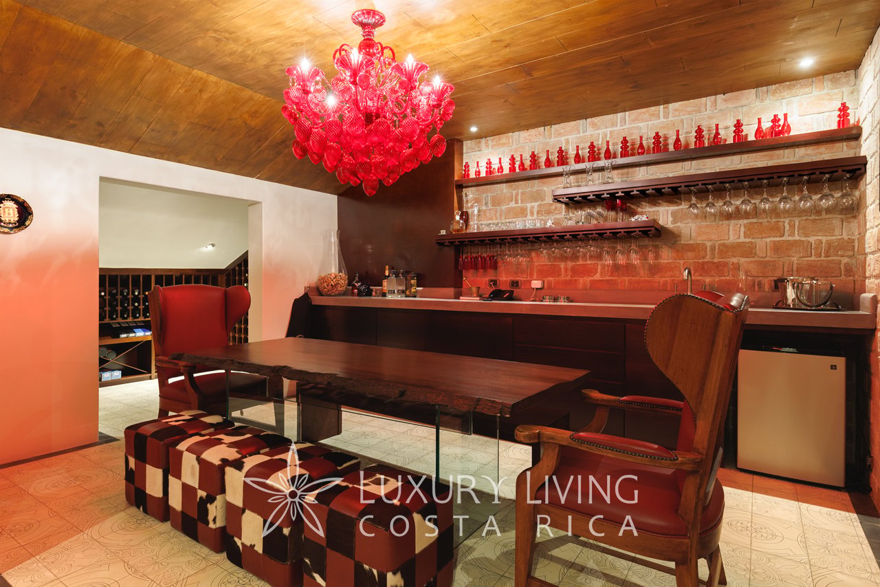 Dining area with a red chandelier, dark wood table, leather chairs, and brick bar wall.