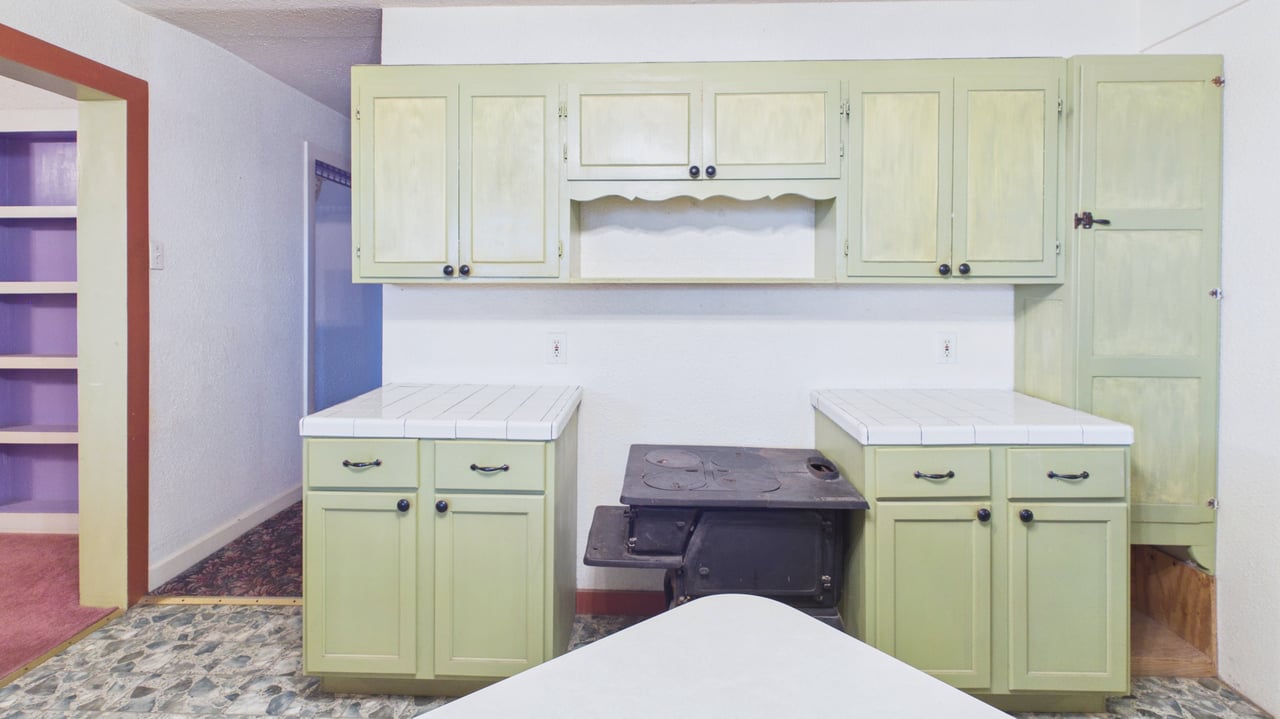 Kitchen with pale green cabinets, white counters, and a black wood-burning cookstove.