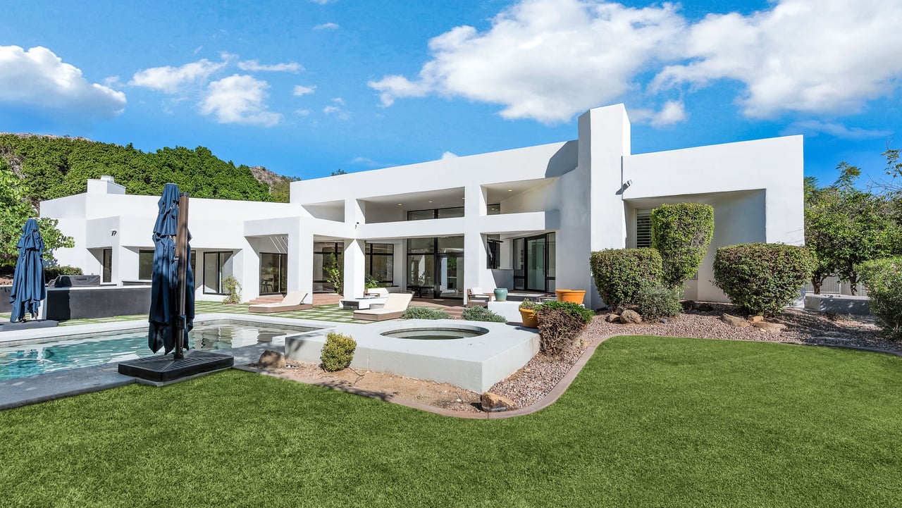 Modern white home with a pool, raised spa, covered patio, and lawn.
