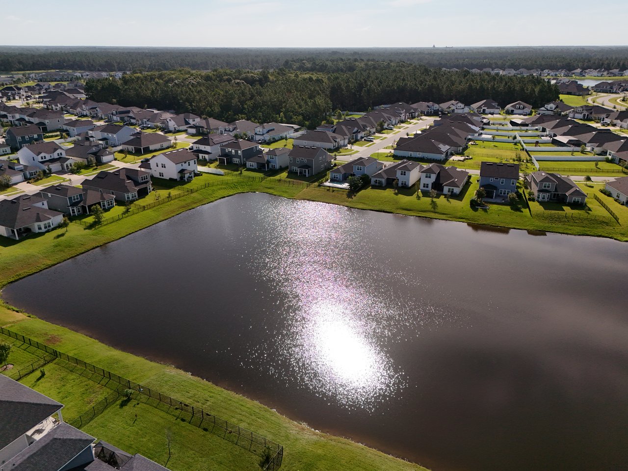 Aerial view of homes lining a pond, with sunlight reflecting across the water.