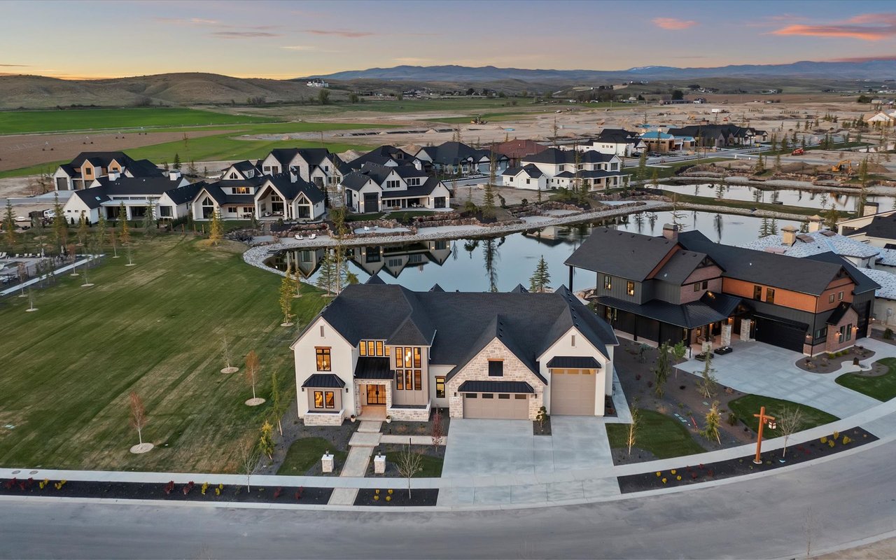 Northwest aerial shot of the home with large green space to the left, the lake behind and the foothills and mountains in the background