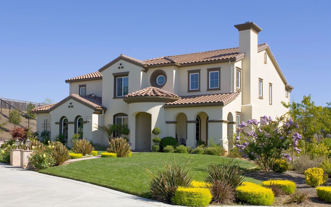 Two-story stucco home with a tiled roof, arched porch, and landscaped front yard.