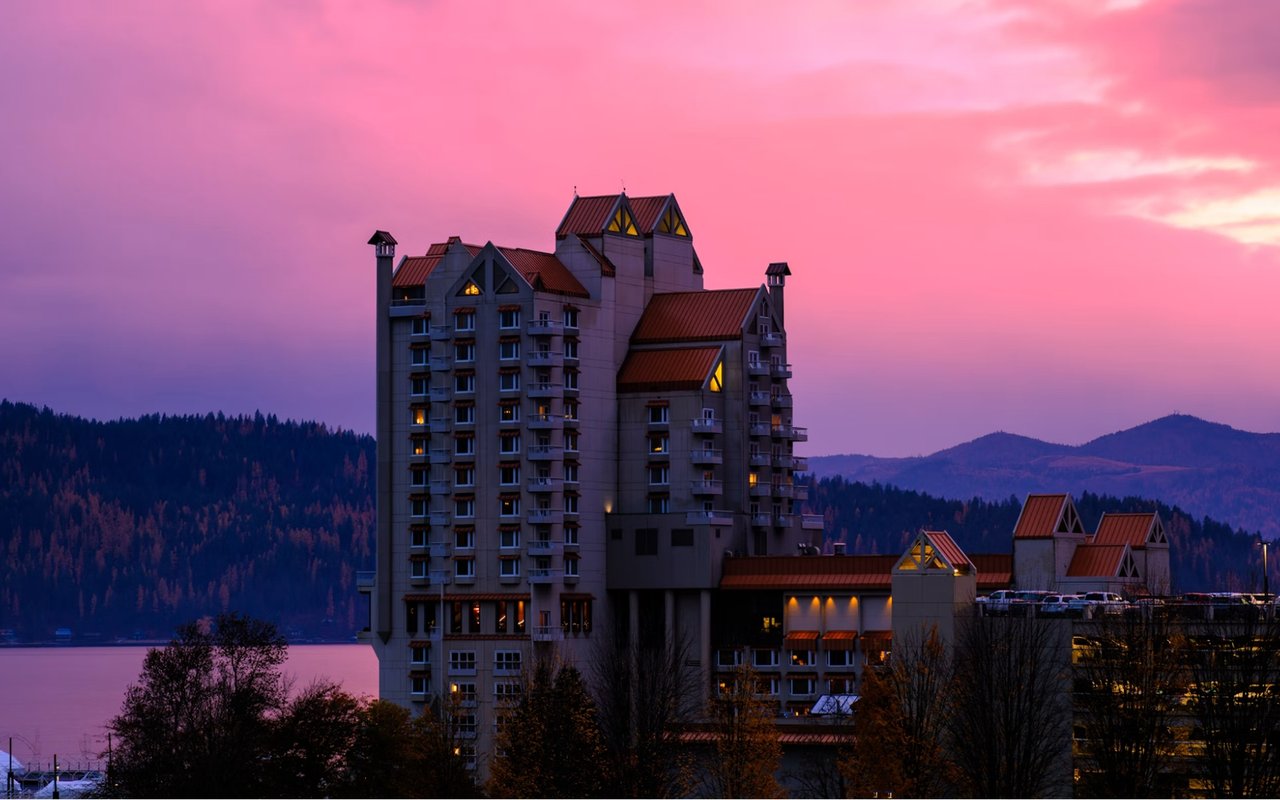 Coeur d'Alene Resort beside the lake at dusk, beneath a vivid pink sky.
