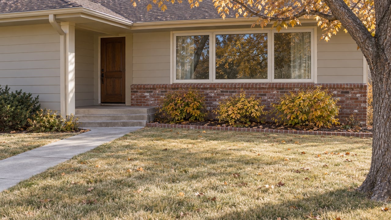 Autumn light on a ranch home's covered entry, brick accents and broad front lawn beneath a mature oak.
