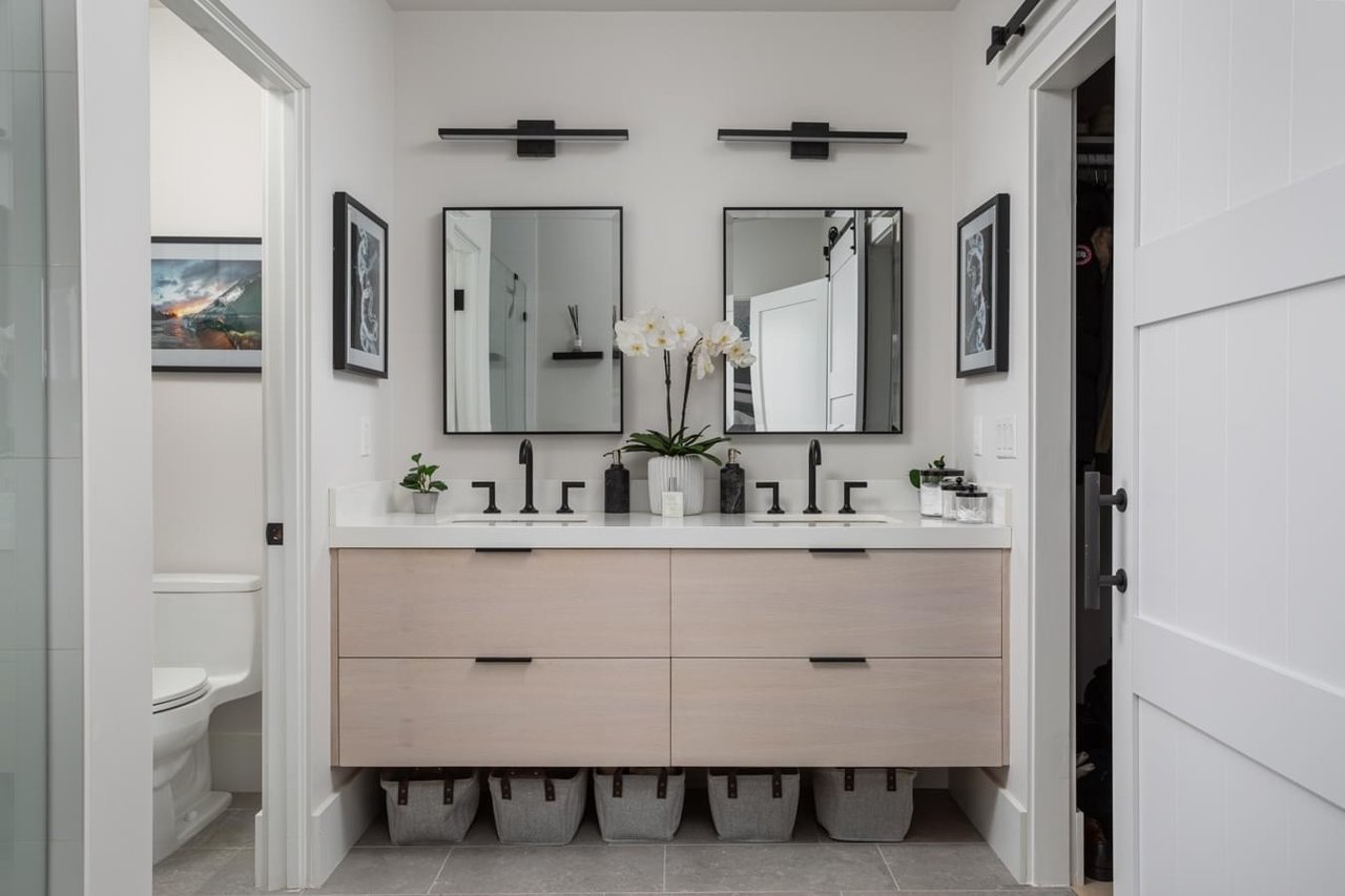  A modern bathroom featuring a light wood double vanity with a white countertop and a pair of square mirrors above the sinks.