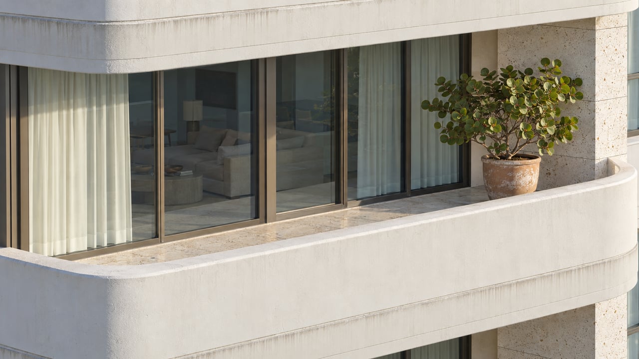 Close architectural photograph of a curved ivory concrete condo terrace, bronze-framed glazing, shell-flecked limestone and a single sea grape specimen.