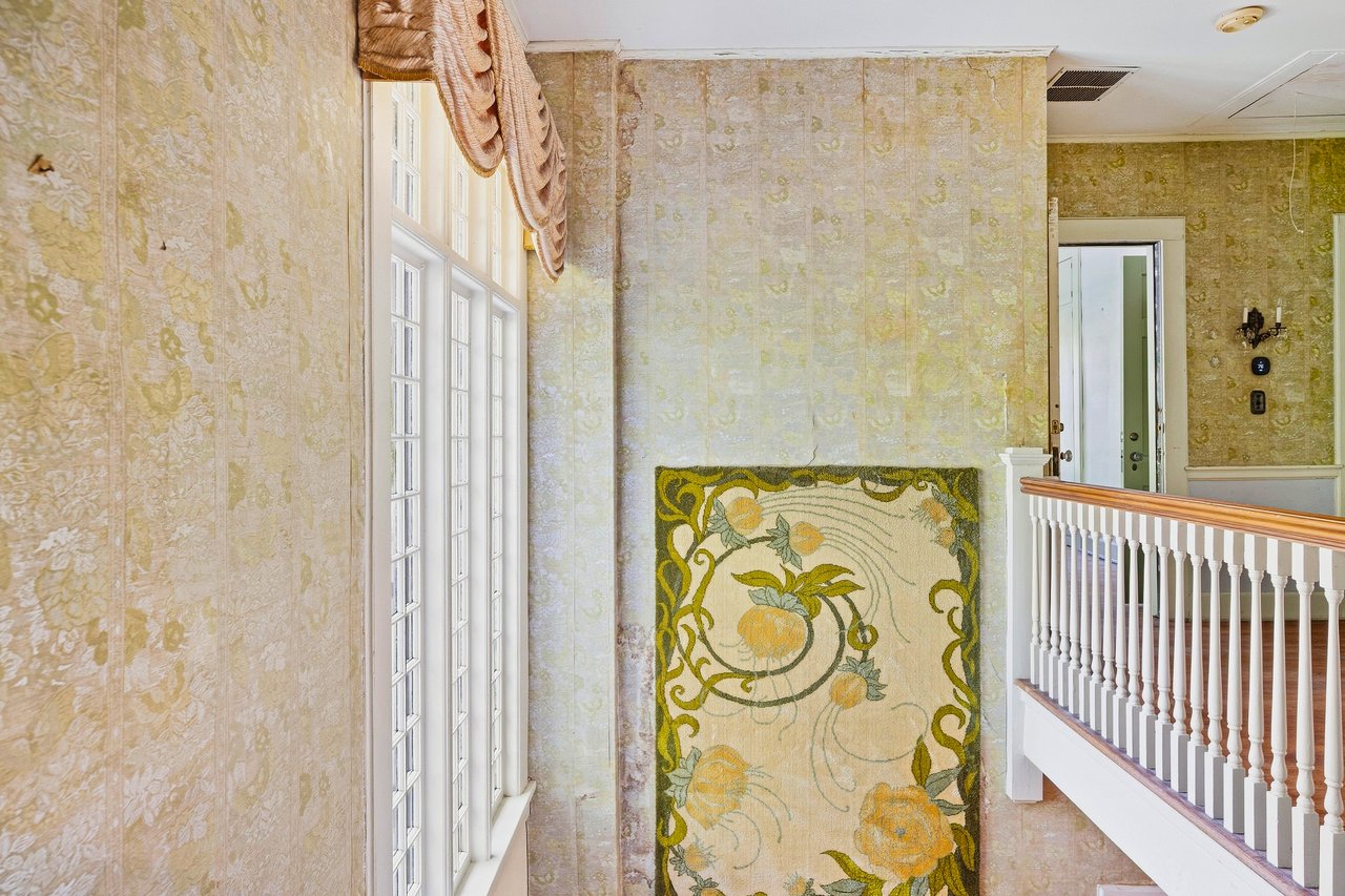 Ornate stair hall with a white balustrade, tall windows, and a floral wall hanging.