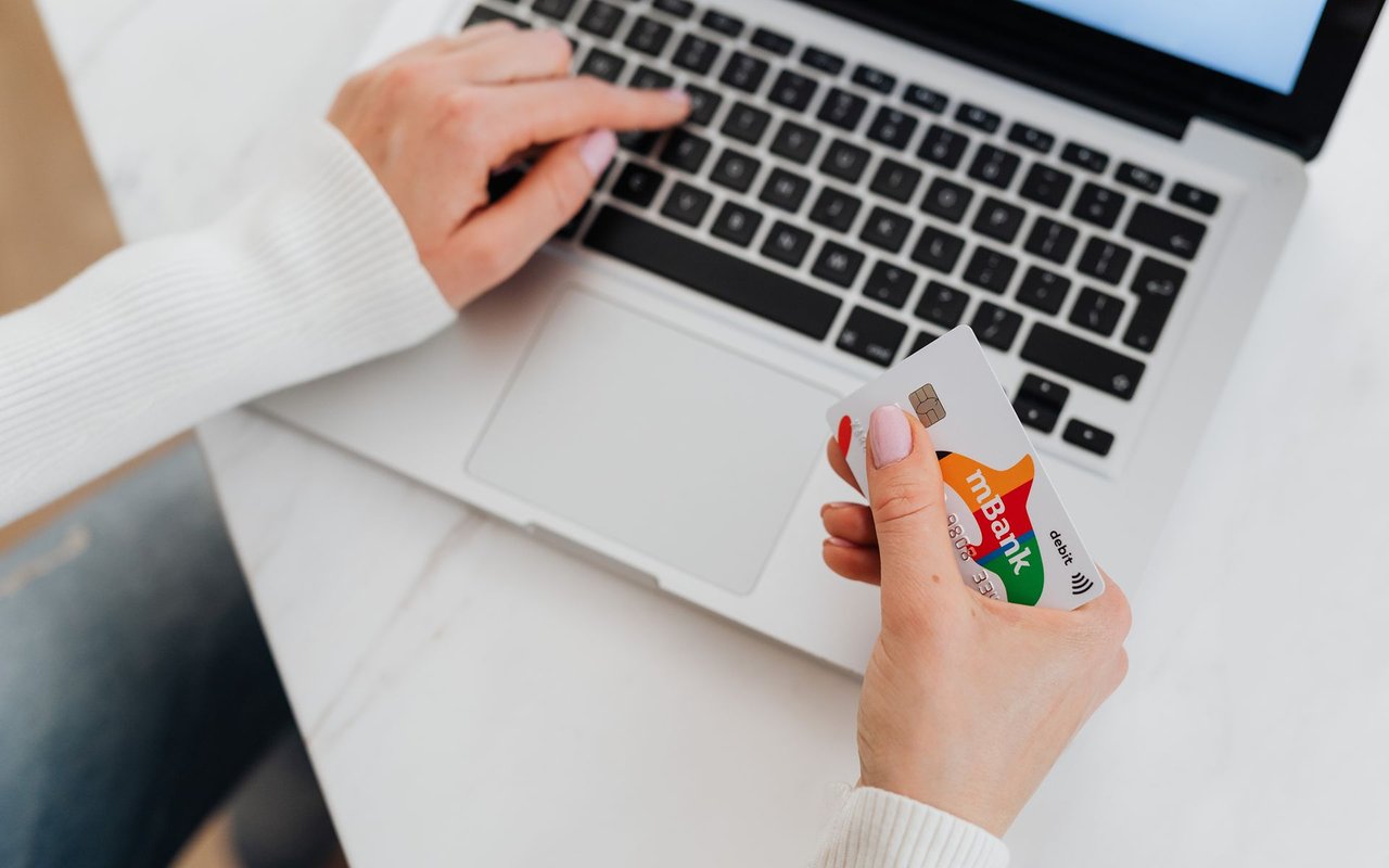 Hands hold a debit card beside a laptop keyboard.
