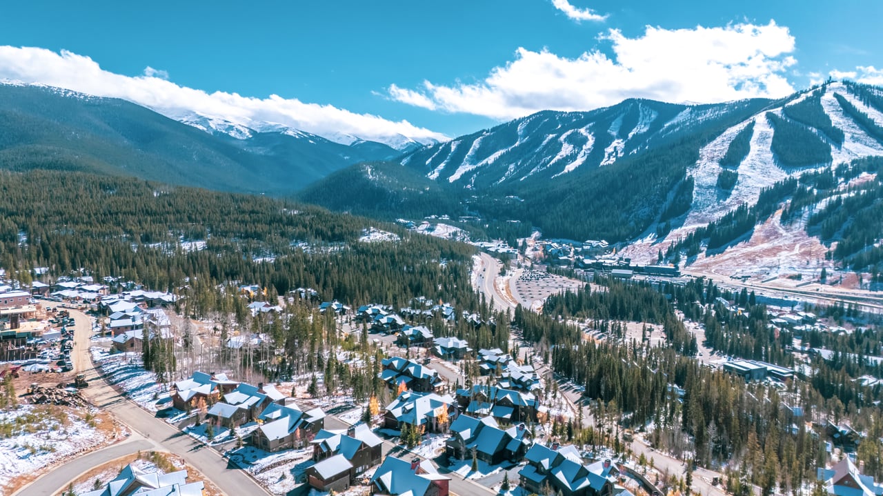 Mountain resort homes among evergreens, with ski runs crossing the snow-dusted peaks above.