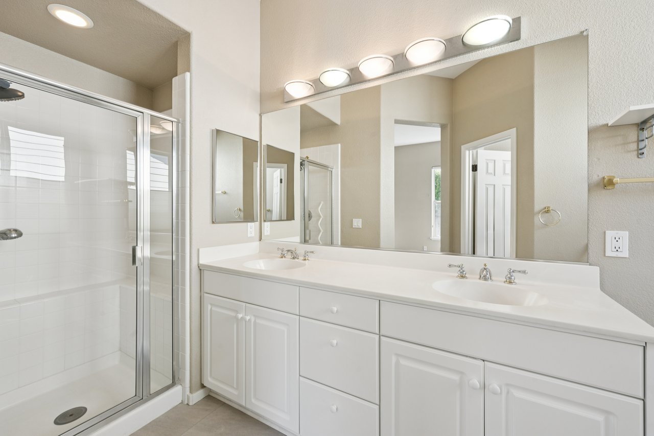 Bathroom with a glass shower and white double-sink vanity beneath a long mirror.