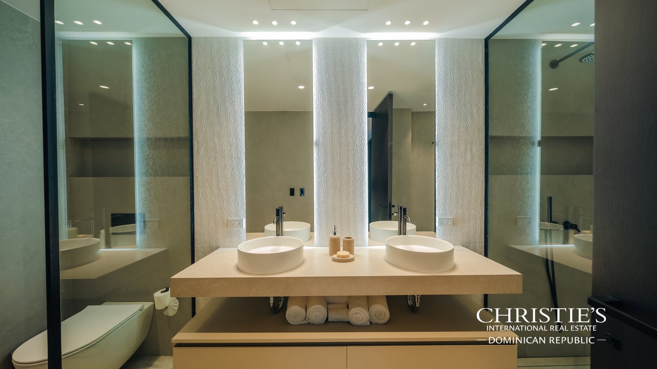 Bathroom with twin vessel sinks, illuminated mirrors, and a glass-enclosed shower.