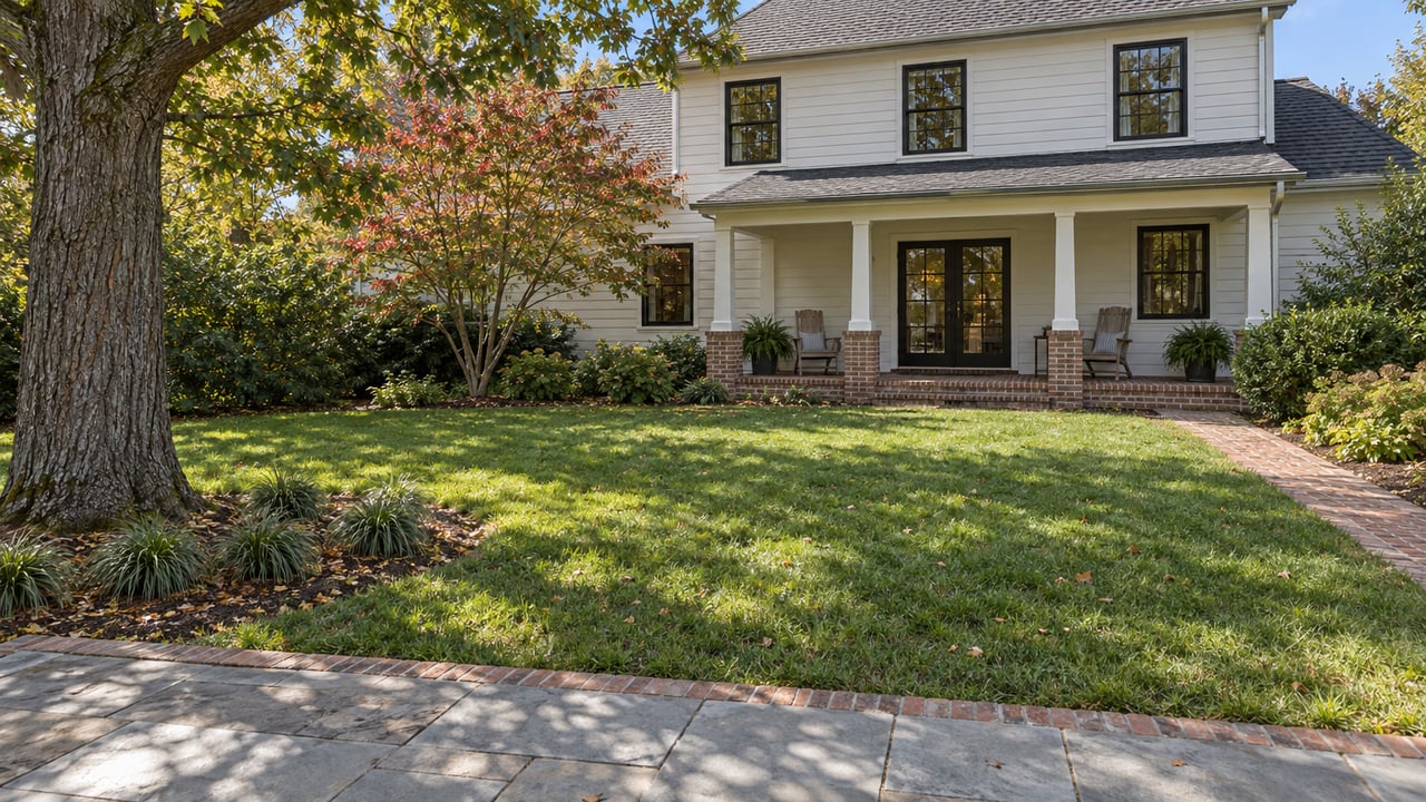 An established white clapboard home with a covered back porch overlooks a deep lawn, mature oak and stone terrace.