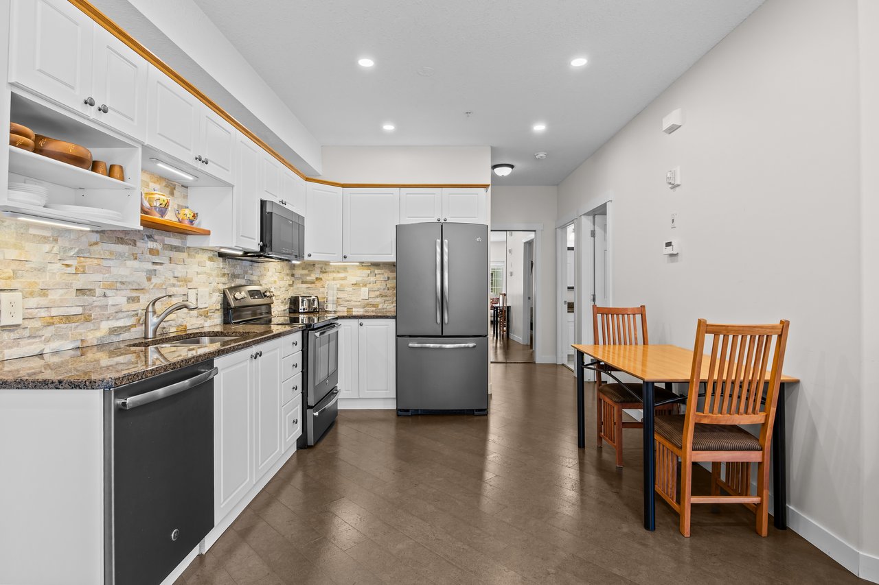 Kitchen with white cabinets, stone backsplash, stainless steel appliances, and a wooden dining table.