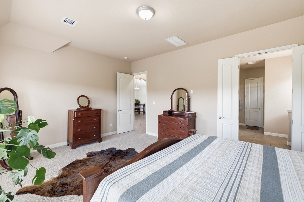 Furnished bedroom with a striped bedspread, dark wood dressers, and open doors to a tiled hallway.