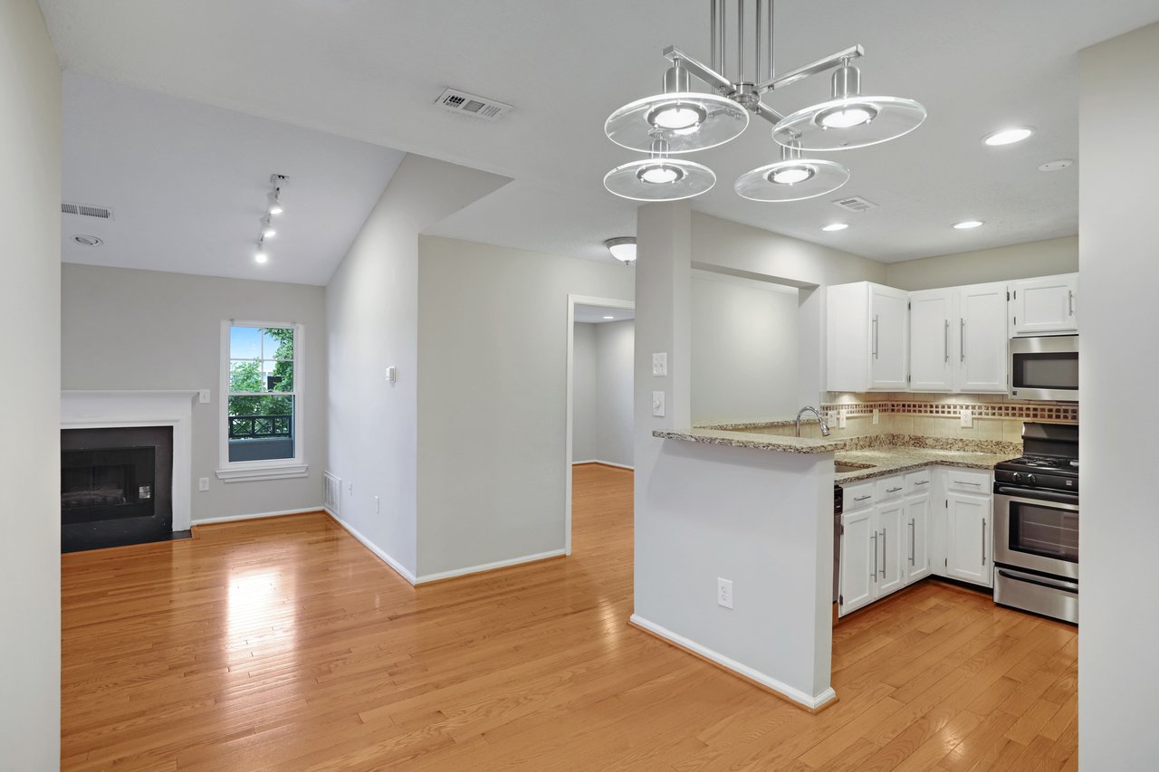 Open-plan living room and kitchen with hardwood floors, a fireplace, and white cabinets.